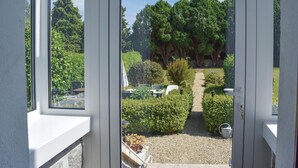 A view through a door of a garden with a gravel path, potted plants, and a seating area with chairs and tables.
