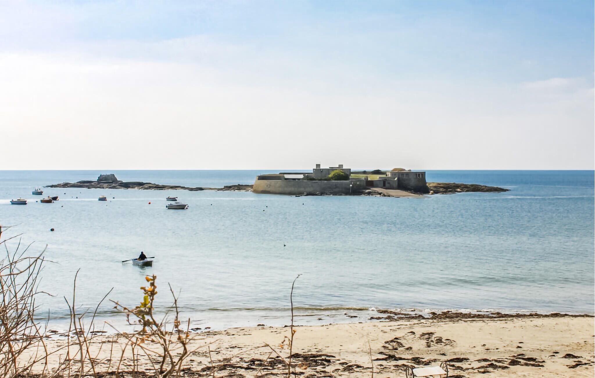 Eine Küstenlandschaft mit einer befestigten Anlage, Booten und einem Sandstrand.