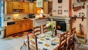 A cozy kitchen with wooden cabinets, a dining table set with chairs, a fireplace, and various kitchen appliances. - 3 bedroom amazing home in Riantec (Riantec)