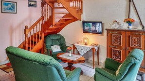 A cozy living room with a wooden staircase, green armchairs, a small table with a vase, and a cabinet with decorative items. - 3 bedroom amazing home in Riantec (Riantec)