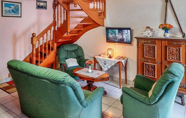 A cozy living room with a wooden staircase, green armchairs, a small table with a vase, and a cabinet with decorative items. - 3 bedroom amazing home in Riantec (Riantec)