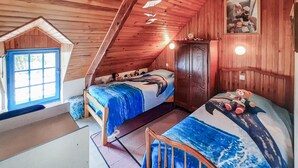 A cozy cabin-style bedroom with a sloped ceiling, a bed with a dolphin-themed bedspread, a small wooden chair, and a window with a blue frame. - 3 bedroom amazing home in Riantec (Riantec)