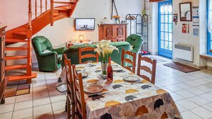 A dining area with a table set for two, surrounded by green upholstered chairs. A wooden staircase is visible to the left, and a blue door is in the background. - 3 bedroom amazing home in Riantec (Riantec)