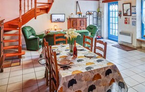 A dining area with a table set for two, surrounded by green upholstered chairs. A wooden staircase is visible to the left, and a blue door is in the background. - 3 bedroom amazing home in Riantec (Riantec)