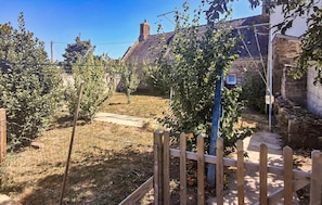 Un jardin entouré d’une clôture en bois, d’un mur de pierre et d’une maison dont le toit est recouvert de tuiles.