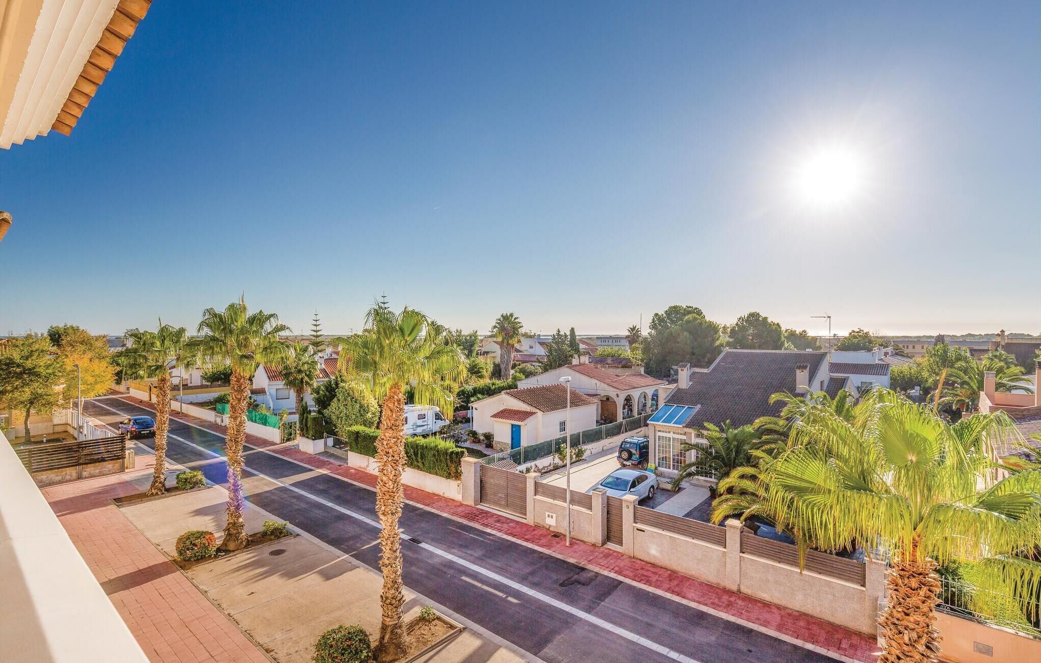 A residential area with palm trees, a clear sky, and a street with parked cars.