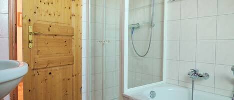 A bathroom with a wooden door, a glass shower enclosure, a bathtub, and a sink.
