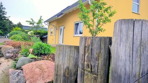 A yellow house with a wooden fence, a small tree, and a garden with rocks and plants.