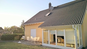 A house with a tiled roof, a covered patio with chairs, and a garage door.