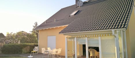 Et hus med tegltag, en overdækket terrasse med stole og en garageport.