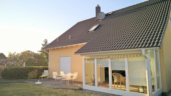 A house with a tiled roof, a covered patio with chairs, and a garage door.