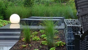 Un jardín en la azotea con una luminaria esférica, jardineras elevadas y una valla de metal.