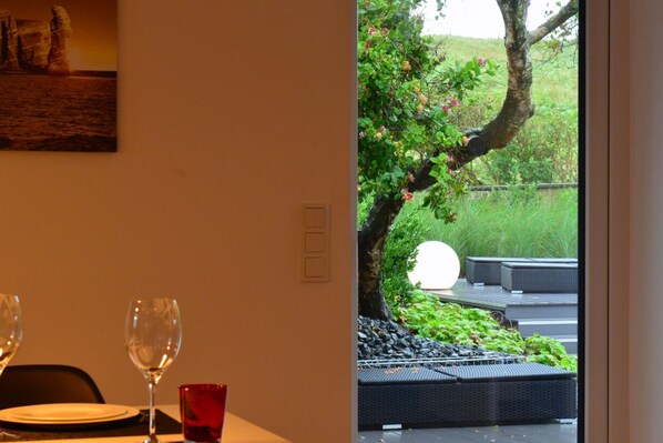 A dining area with a table set for two, a glass of red wine, and a painting on the wall. - House - House Sathurn (Helgoland)