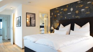 Un dormitorio moderno con una cama grande, un cabecero oscuro y un mural de peces y barcos.