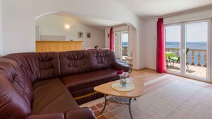 A living room with a brown leather sofa, a small round table with a vase, and a view of the sea through large sliding glass doors. - Holiday apartment with pool and sea view (Dramalj)