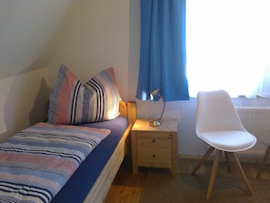 Ett sovrum med en säng, ett nattduksbord, ett skrivbord, en stol och ett fönster med gardiner.