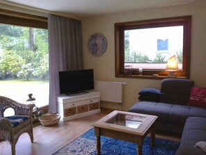 A living room with a television, sofa, and a window with a view of trees.