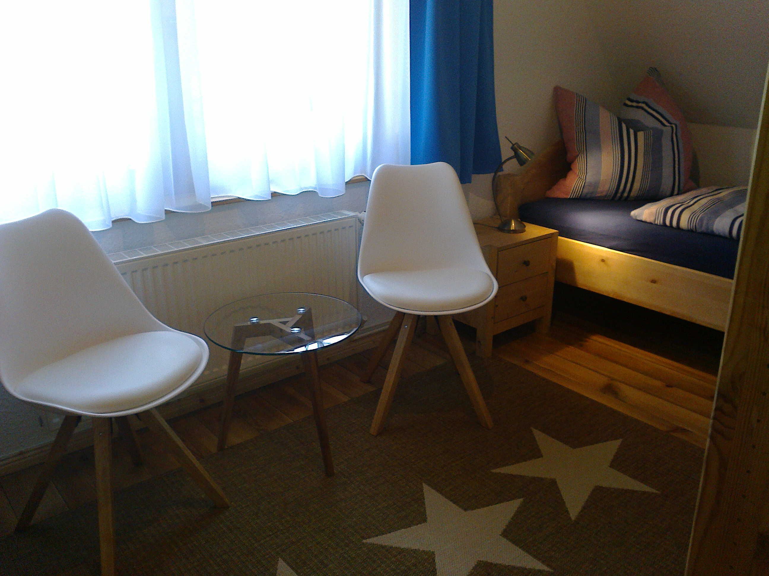 Ett rum med en säng, två vita stolar, ett litet bord, en lampa och en matta med stjärnmönster.