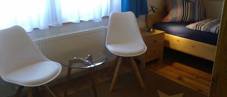 Ett rum med en säng, två vita stolar, ett litet bord, en lampa och en matta med stjärnmönster.