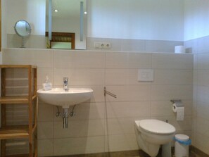 A bathroom with a sink, mirror, toilet, and a trash bin.