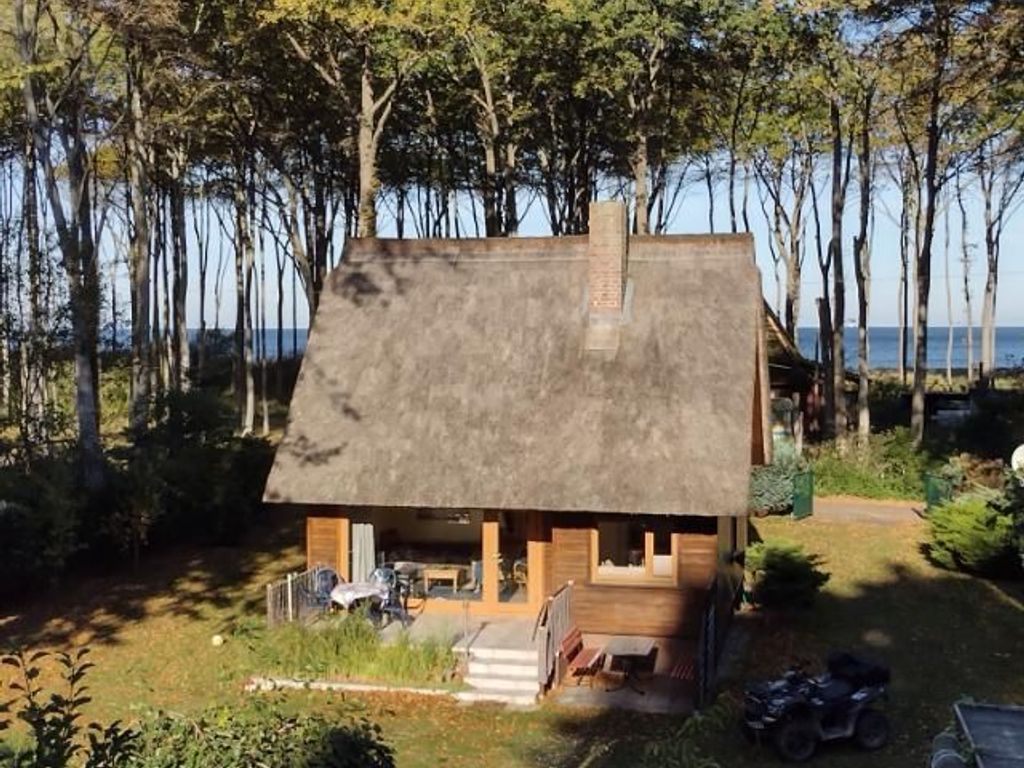Ein kleines, rustikales Blockhaus mit Strohdach, umgeben von Bäumen und freiem Blick auf das Wasser.