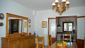 A dining room with a wooden table, chairs, a chandelier, and a kitchen visible through an open doorway. - Stunning home in Estellencs (Estellencs)