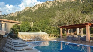 A pool area with lounge chairs, a stone structure, and a view of a mountainous landscape. - Stunning home in Estellencs (Estellencs)