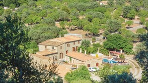A stone building with a tiled roof, surrounded by dense greenery and a swimming pool with a small boat. - Stunning home in Estellencs (Estellencs)