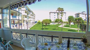 Uma varanda com vista para uma área residencial, uma mesa com jornais e uma cadeira.