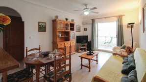 Uma sala de estar com uma mesa de jantar de madeira, cadeiras, um sofá, uma televisão e um ventilador de teto.