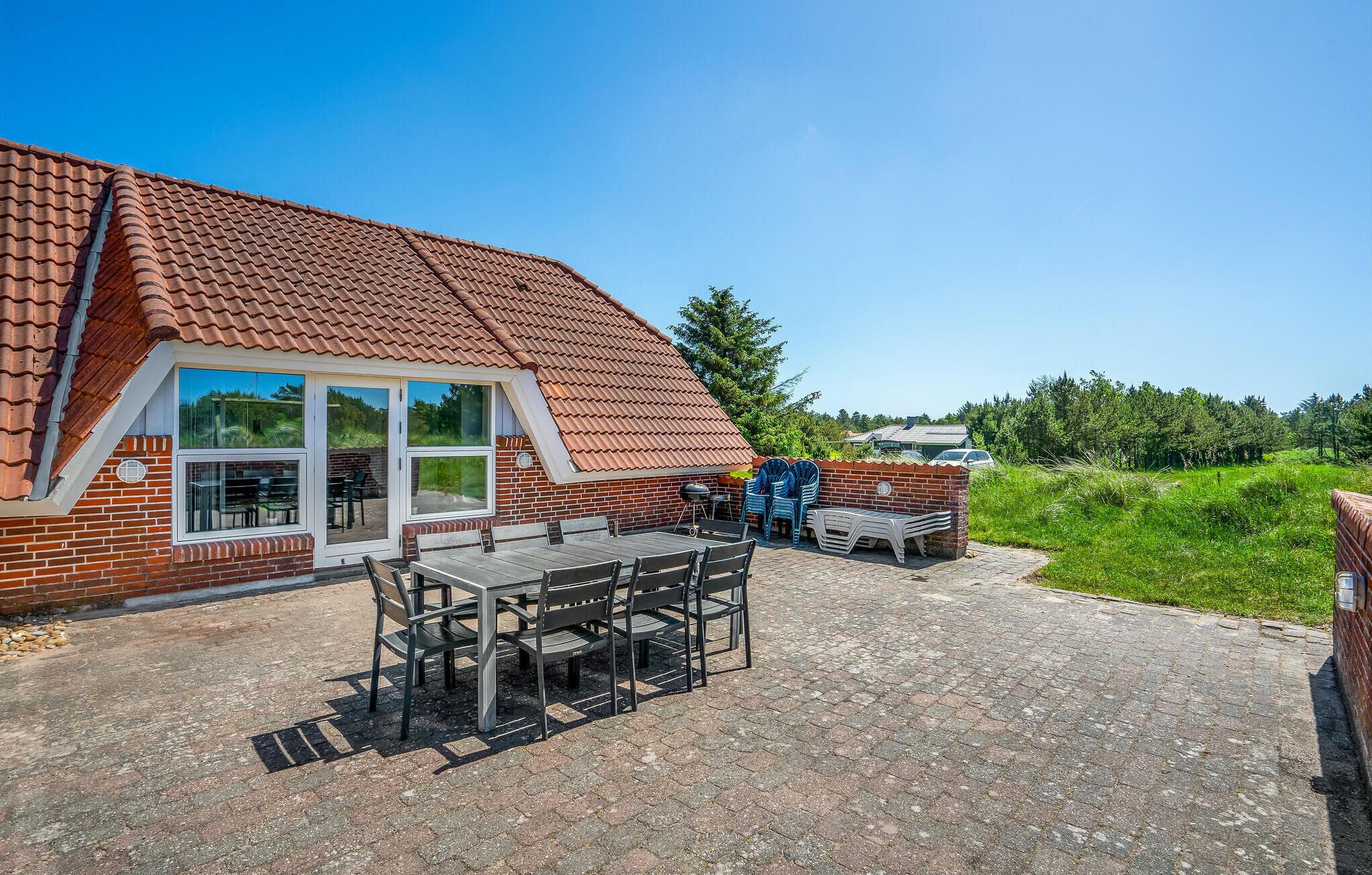 Une maison avec un toit en tuiles, une façade en briques et un patio comprenant une table et des chaises.