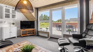 A modern living room with a TV, comfortable seating, a wooden ceiling, and large sliding glass doors to an outdoor patio. - Cozy home in Blåvand with sauna (Blåvand)