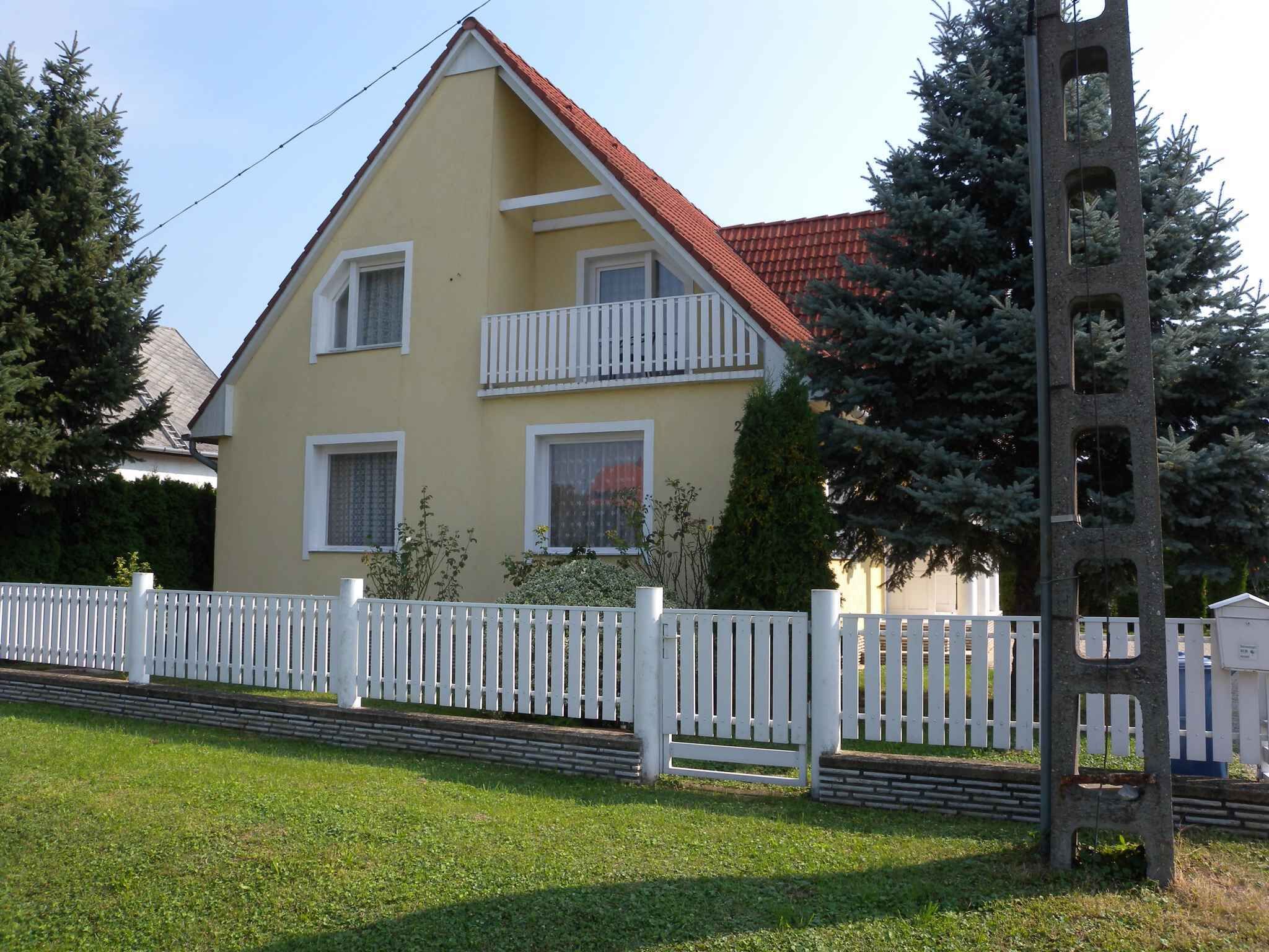 A two-story house with a red roof, white exterior, and a white picket fence.
