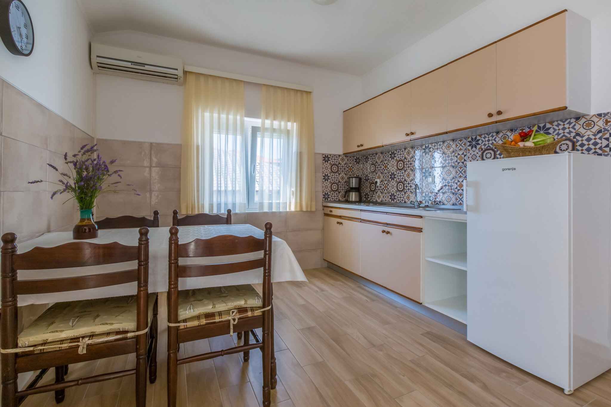 Eine Küche mit Esstisch, Stühlen, einem Kühlschrank und einem Fenster mit Vorhängen.