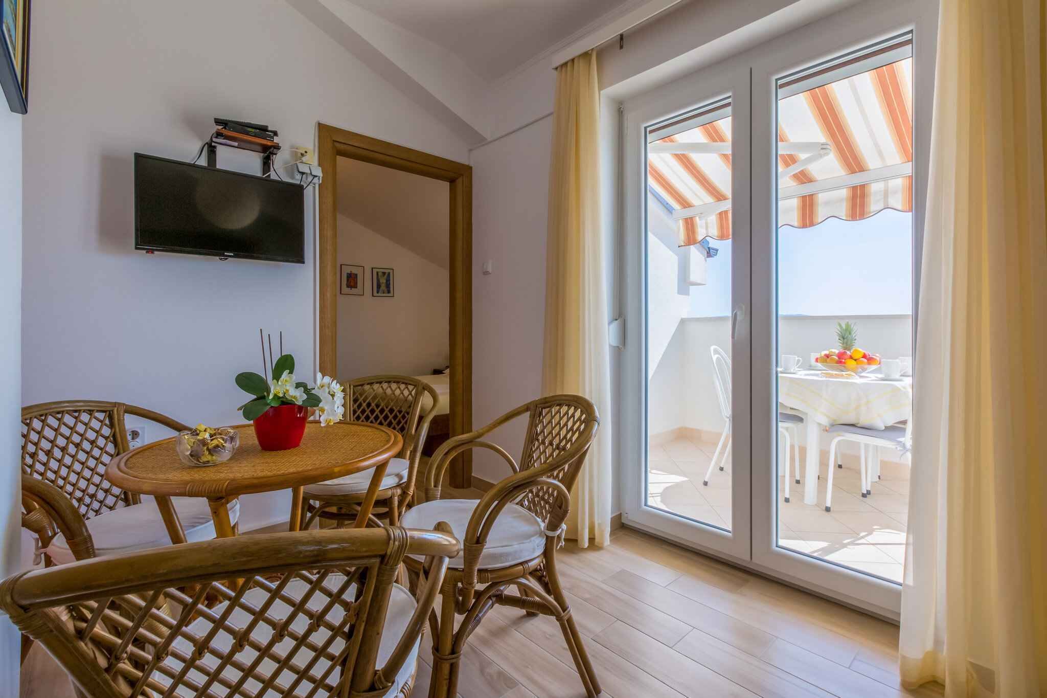 Une pièce comprenant une table à manger et des chaises, un téléviseur à écran plat fixé au mur, et une porte-fenêtre coulissante donnant sur un espace extérieur avec une table et des chaises.
