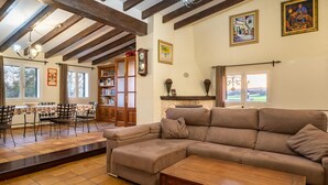 A cozy living room with a sectional sofa, a wooden coffee table, and a fireplace. There is a bookshelf filled with books and a dining area with a table and chairs. - Awesome home in Sineu (Sineu)