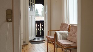 Un couloir doté d’un plancher en bois, une porte donnant sur l’extérieur et deux chaises avec des coussins à rayures.