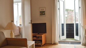 Un salon avec un téléviseur posé sur un meuble en bois, un canapé, une lampe et une porte-fenêtre coulissante donnant sur un espace extérieur.