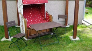 A wooden outdoor seating area with a red polka dot table and chairs, a woven chair with a red canopy, and a concrete base. - Apartment Zum Kölpinsee - K��lp - Will (Loddin)
