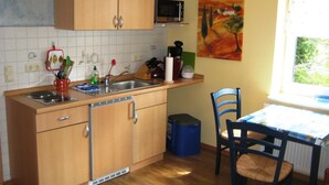 A kitchen with wooden cabinets, a microwave, a sink, and a dining area with a table and chairs. - Apartment Zum Kölpinsee - K��lp - Will (Loddin)