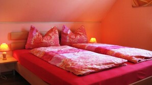 A bedroom with two beds, each with a red bedspread and pink pillows. There is a nightstand with a lamp on each side of the beds. - Apartment Zum Kölpinsee - K��lp - Will (Loddin)