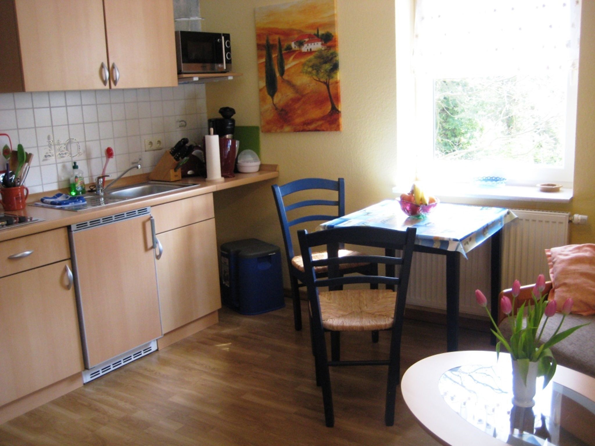Une cuisine compacte avec des meubles en bois, un four à micro-ondes et un évier. On y trouve une table à manger avec des chaises et une fenêtre qui laisse entrer la lumière naturelle.
