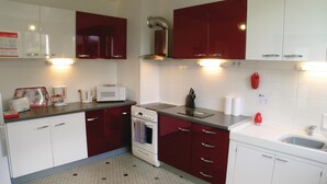 A compact kitchen with white and red cabinets, a microwave, a kettle, a toaster, and a stove.