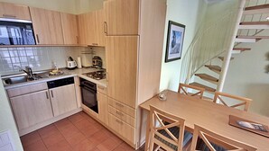 A compact kitchen with wooden cabinets, a dishwasher, a stove, and a dining table with chairs. - Vacation apartment 1.2.14 Inselstrand - Holiday apartment 1.2.14 (Heringsdorf)