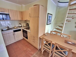 Una cucina compatta con mobili in legno, lavastoviglie, piano cottura e tavolo con sedie.