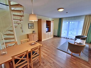A spacious room with a wooden dining table, chairs, a spiral staircase, a cabinet, and a large window with curtains.