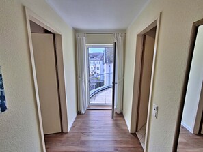 A corridor with wooden flooring leading to a balcony with a view of buildings.