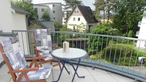 A balcony with a round table and two wooden chairs, one with a newspaper cushion. - Vacation apartment 1.2.14 Inselstrand - Holiday apartment 1.2.14 (Heringsdorf)