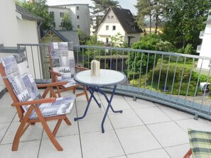 Un balcone con un tavolo rotondo e due sedie di legno, una con cuscino porta giornale.