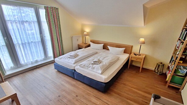 A hotel room with a large bed, two bedside tables with lamps, a small table, and a bookshelf. - Vacation apartment 1.2.14 Inselstrand - Holiday apartment 1.2.14 (Heringsdorf)